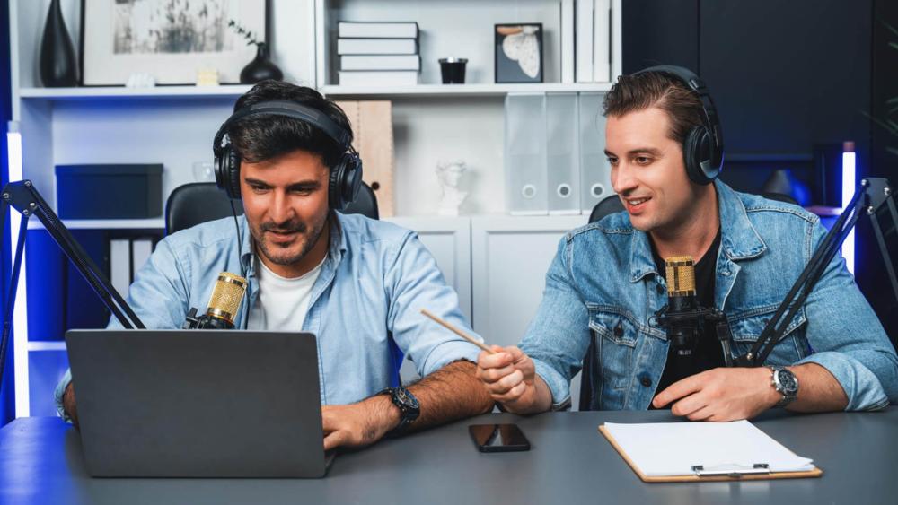 Two men recording a podcast using AI laptops and microphones.