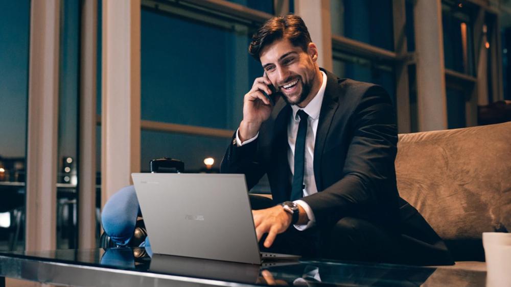 Business professional using an ASUS laptop while on a phone call in a modern office or lounge setting