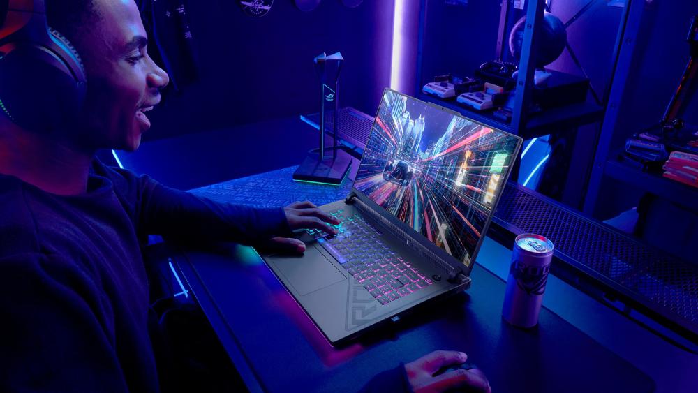 Gamer using an ASUS ROG laptop with RGB keyboard lighting in a neon-lit setup, playing a high-speed racing game.