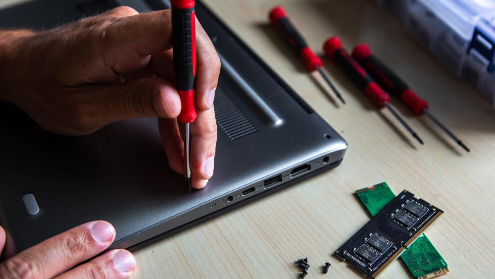 Technician opening laptop base to access RAM and storage components