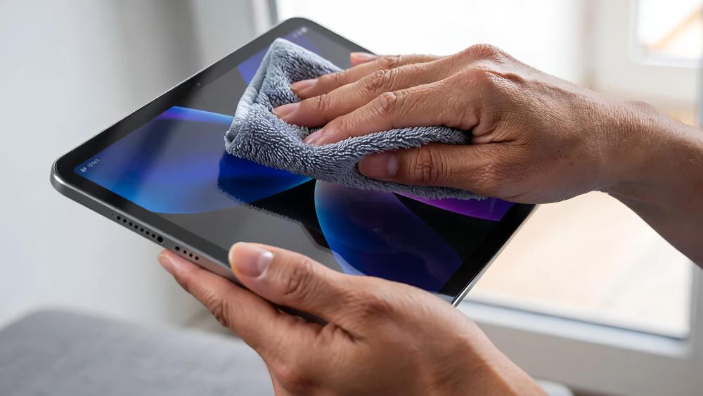 Person cleaning a 10-inch tablet screen using a microfibre cloth
