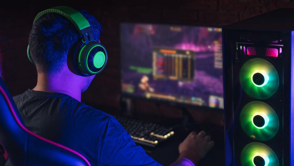 Gamer wearing a headset playing on an RGB gaming desktop PC with illuminated cooling fans