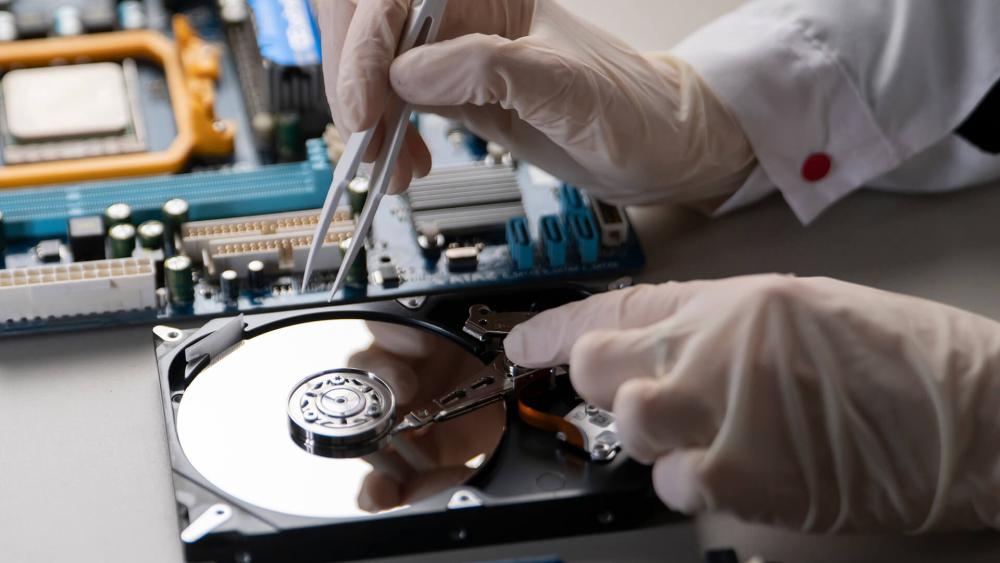 Technician repairing hard disk drive with tools near motherboard during data recovery and hardware repair process.