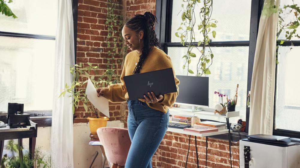 Professional holding HP laptop in a bright plant-filled workspace