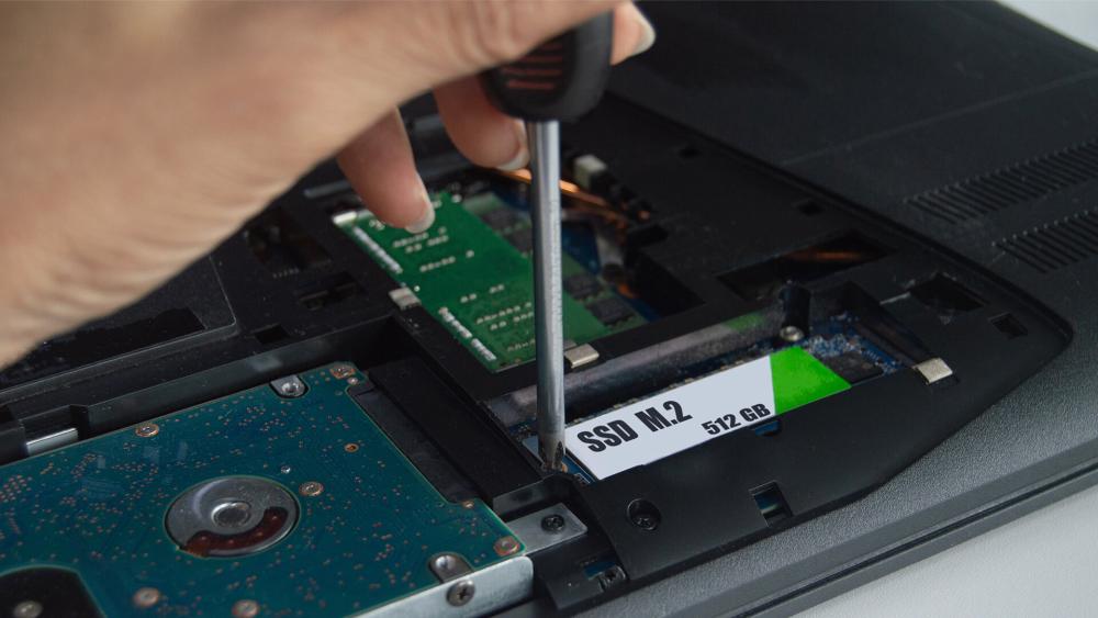 Close-up of installing an M.2 SSD inside a laptop using a screwdriver during a storage upgrade or repair.