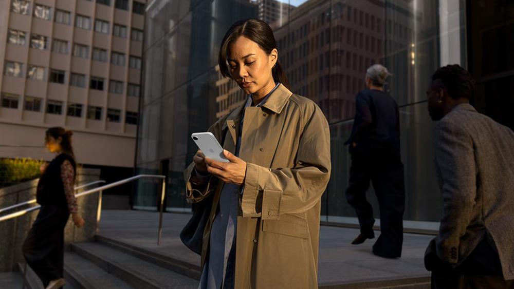 Woman using iPhone 17e outdoors in city setting