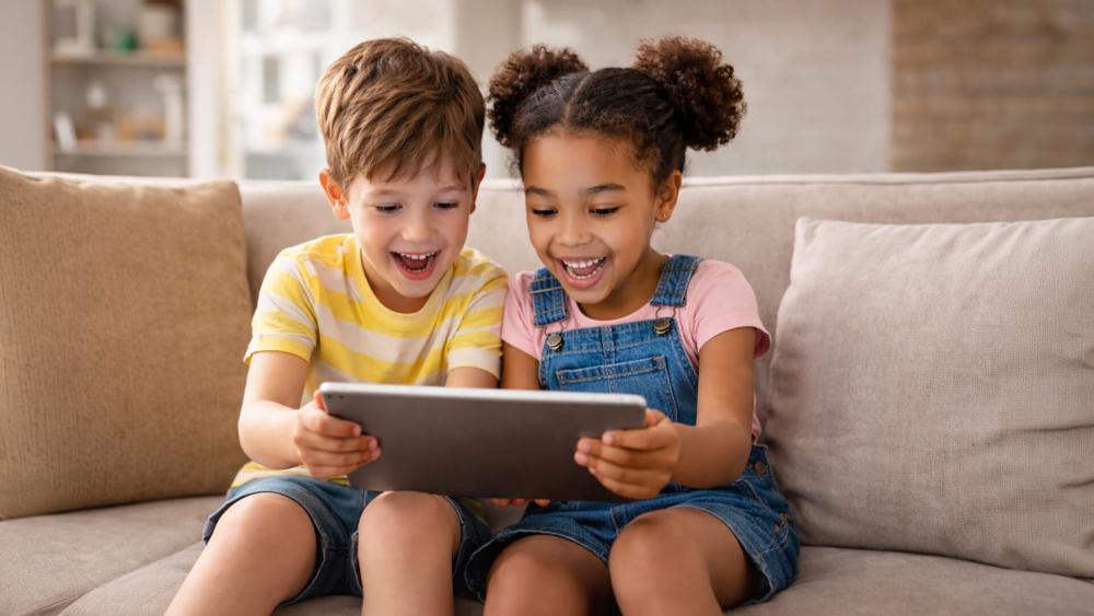 Two children sitting on a sofa using a tablet together for learning and entertainment at home.