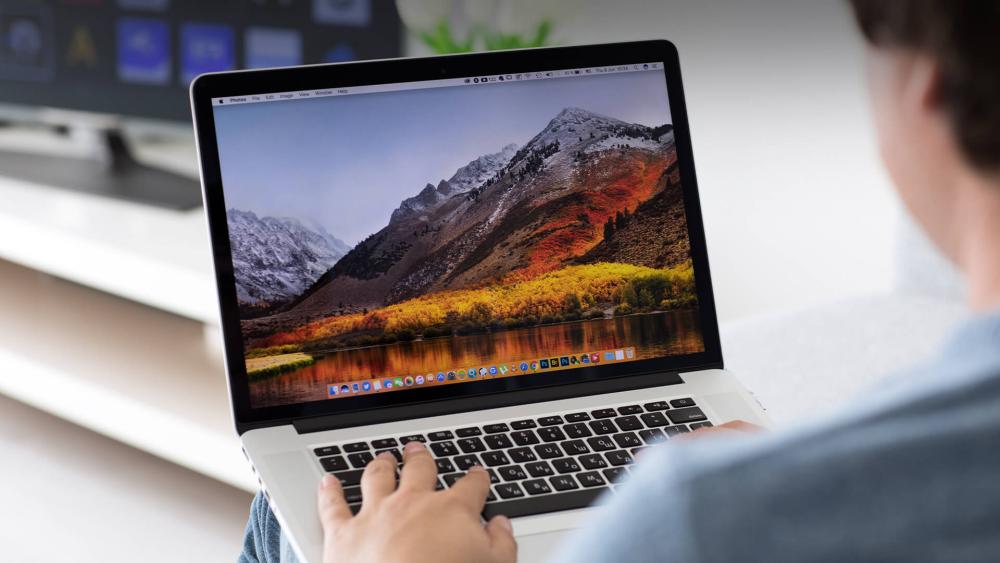Person using a laptop with a mountain landscape wallpaper displayed on the screen.