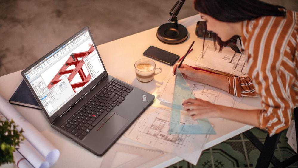 Architect working on technical drawings using a Lenovo ThinkPad laptop with CAD software and blueprints on a desk