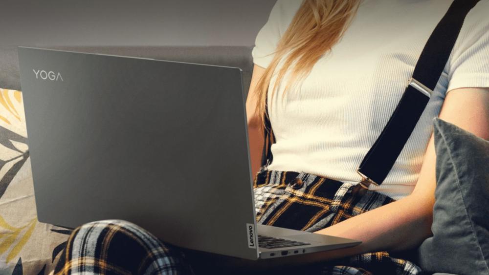 Person using a Lenovo Yoga laptop while sitting on a sofa at home, highlighting slim design and everyday use.