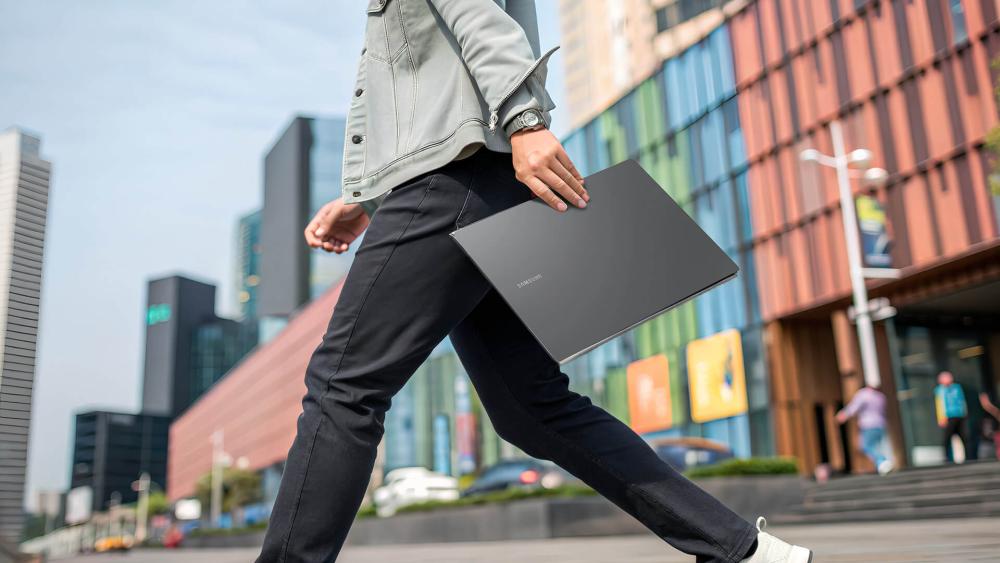 Person carrying a Samsung Galaxy Book laptop while walking outdoors