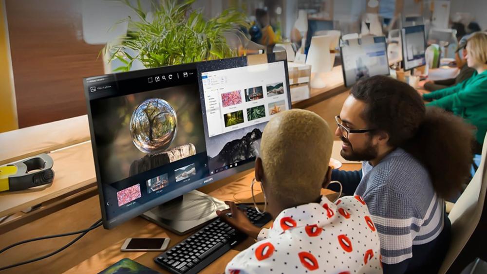 Two professionals collaborating at a modern office desk using a Philips 4K monitor for creative design and productivity tasks