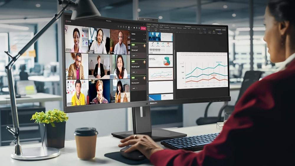 Philips 4K monitor used in a modern office showing video conferencing, charts, and productivity dashboards on a large display
