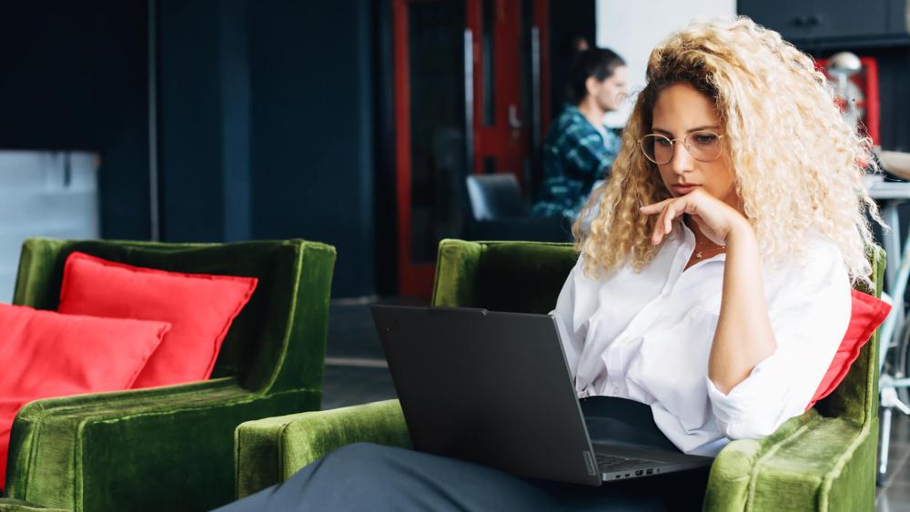 Professional woman working on a laptop while sitting in a modern office lounge area with green chairs.