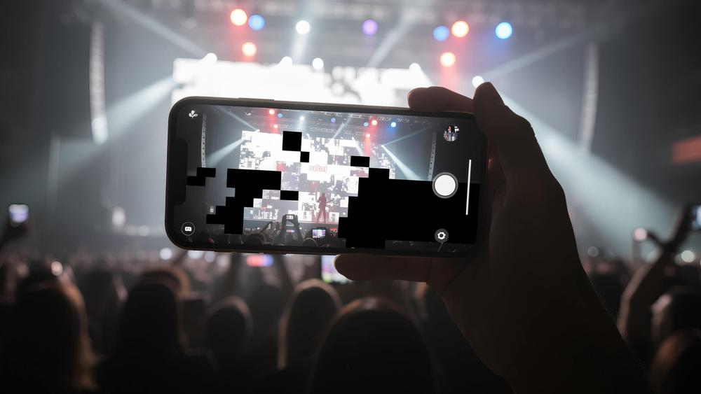 Person recording a live concert on a smartphone with visible pixelated camera glitches on the screen