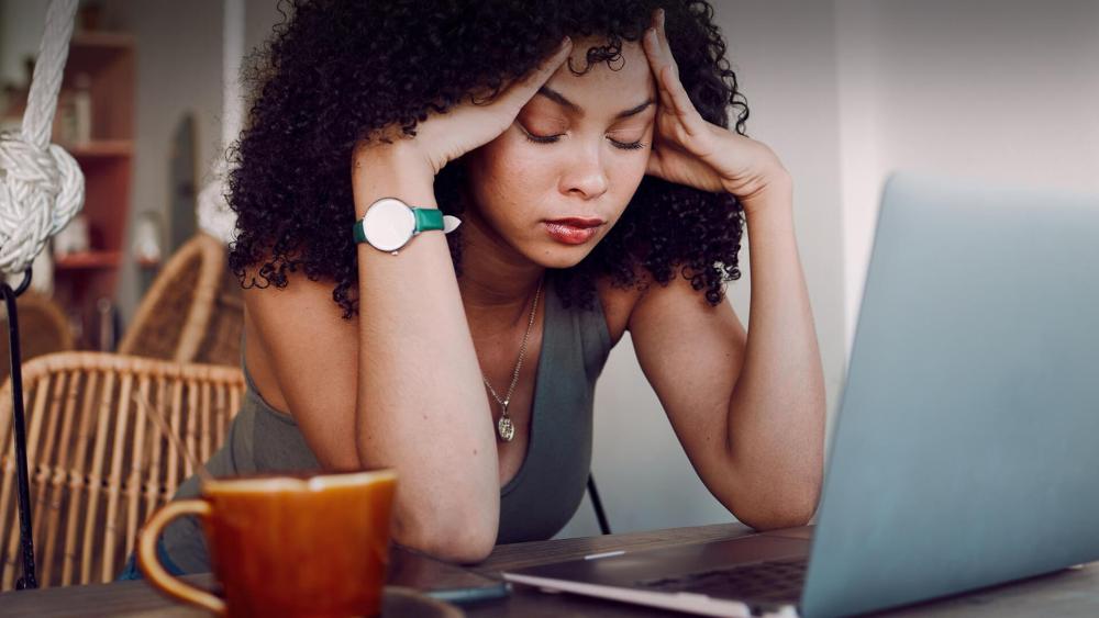 Stressed remote worker sitting at a laptop at home, showing mental fatigue and work from home challenges