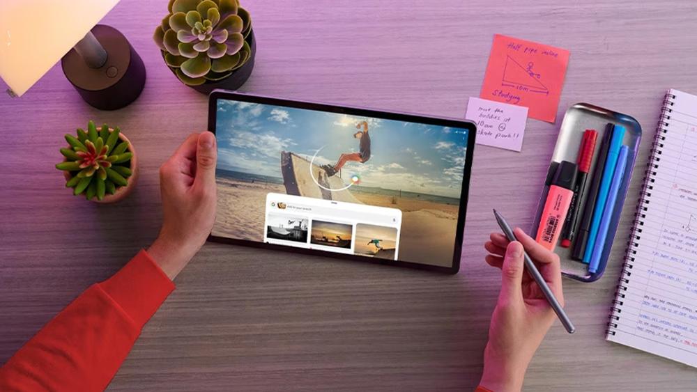 Student using a tablet with a stylus on a desk with study notes, pens and notebook while watching educational content.