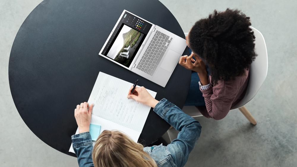Two students studying at a round table with an ASUS laptop open and notes being written in a notebook.