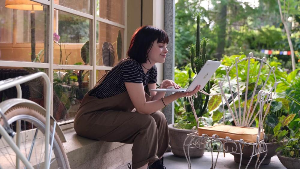 Woman using a laptop outdoors on a porch surrounded by plants, highlighting portable everyday computing and flexible working